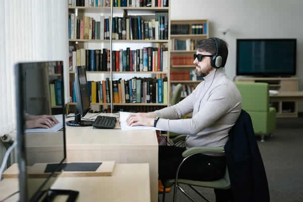 Hombre leyendo en Braille frente a una PC, con auriculares. Servicios de data entry relacionados con accesibilidad